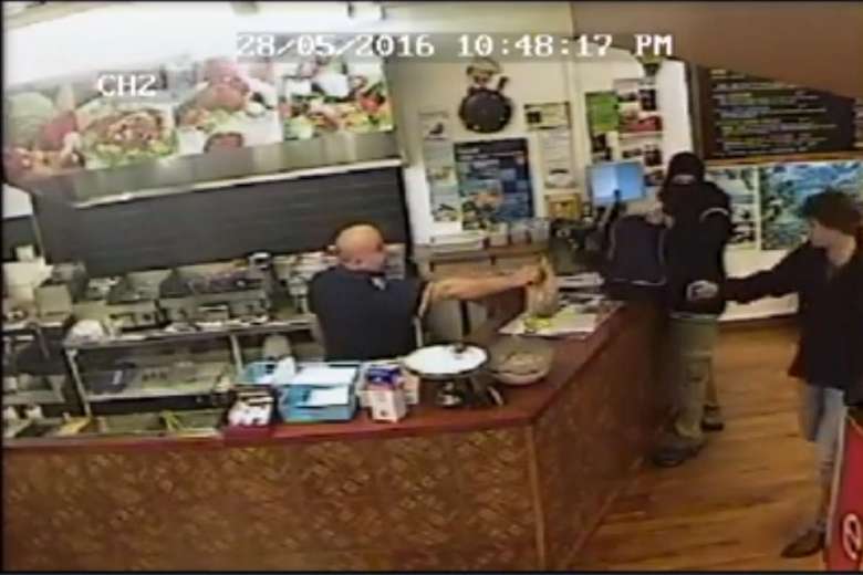 Kebab shop owner Said Ahmed (left) handing a souvlaki to a customer (right) while ignoring an armed robber